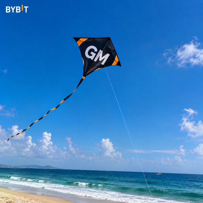 The image shows a beach scene with a kite flying high in the sky, featuring the letters "G" and "M" on its tail. The photo also includes a caption that reads "Bybit #CryptoArk". This suggests that the kite is related to cryptocurrency or digital assets, possibly as part of an event or activity at the beach promoting such products.

The image captures the essence of a sunny day by the ocean with people enjoying their time on the beach and flying kites in the sky. The presence of the kite also adds a sense of fun and leisure to the scene, making it a perfect representation of a relaxing outdoor activity for those who appreciate nature and its beauty.
