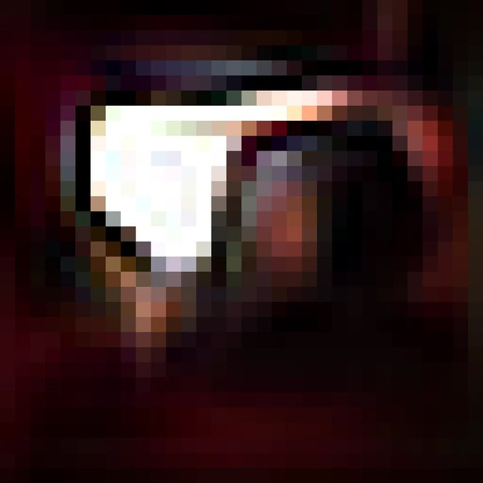 A heavily pixelated image with a dark background and a cluster of bright white and light-colored pixels in the upper-left quadrant.