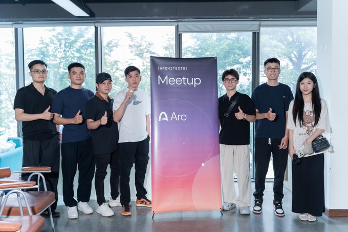 Seven people pose around a pink and purple 'Meetup Arc' banner for Architects at an indoor venue with large windows.