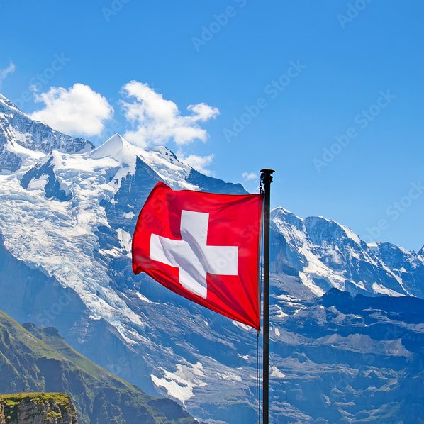 The Swiss flag waving in front of a snow-capped mountain under a blue sky, with an Adobe Stock watermark visible.