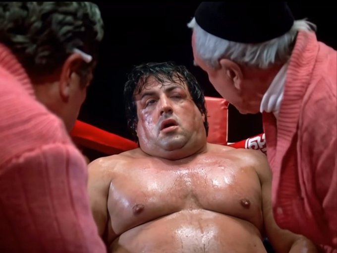 A still from a boxing movie showing a sweaty, exhausted Rocky Balboa being attended to in his corner by his cornermen.