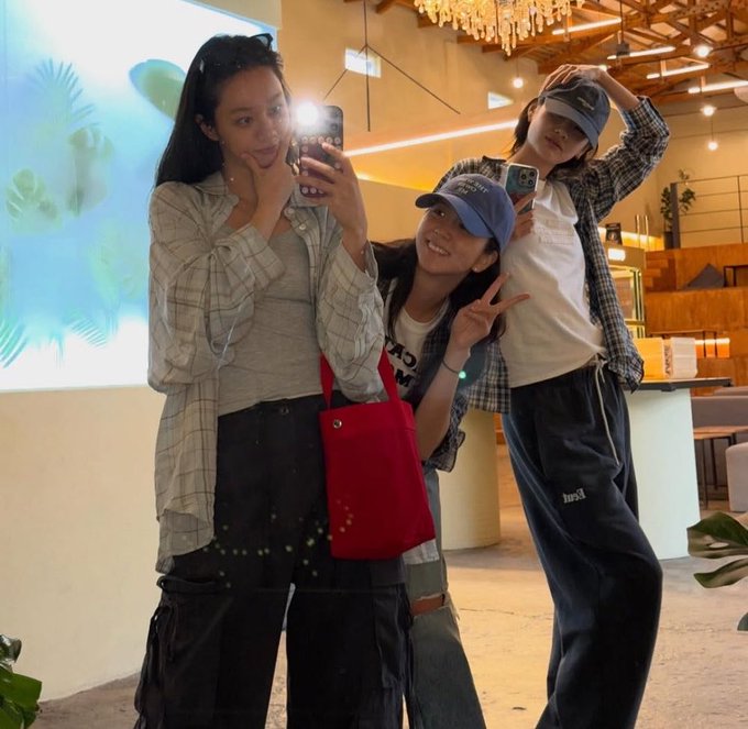 Three friends pose for a mirror selfie in a bright, modern café, with one holding a phone while another flashes a peace sign and wears a navy "hush" cap, capturing a casual celebratory moment that matches the post's upbeat announcement about earning $100 in tips that day.