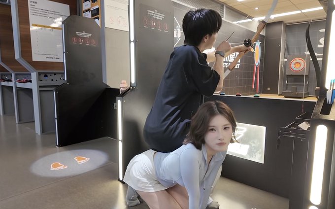 A woman crouches low while a man stands on her back to shoot a bow at an archery target at what appears to be an indoor shooting range. The image humorously illustrates the post's message about unconventional partnerships and extraordinary teamwork being required to achieve great success.