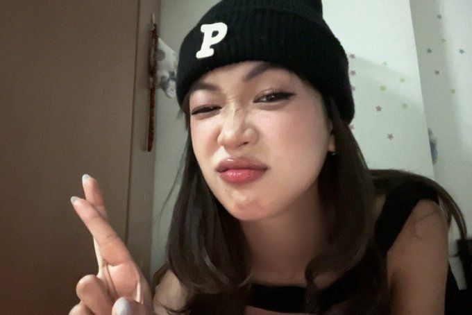 Selfie of a young woman wearing a black beanie with a white 'P' logo, making a peace sign and winking at the camera.