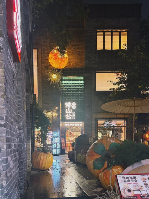 A nighttime street scene featuring a brick building, glowing lantern, and large pumpkin decorations, with a sign reading '佛山地道非遗美食'.