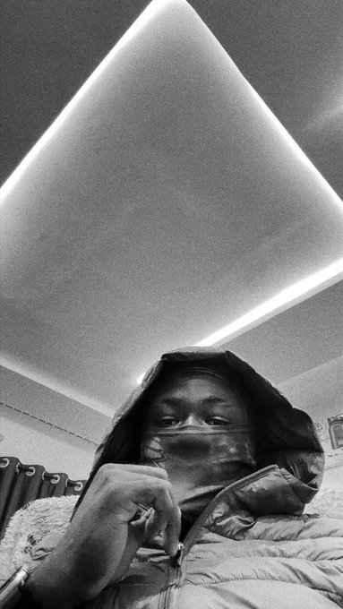 A person bundled in a hooded coat and winter gear takes a selfie under a modern triangular LED ceiling light, appearing cozy indoors while the post reminds them to step outside, reconnect with loved ones, and "touch grass" before the next bull run. The contrast between their warm, sheltered setting and the call to get outside highlights the importance of taking breaks from both the markets and screens.
