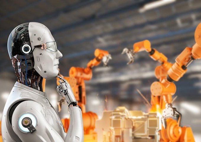A white humanoid robot with a contemplative pose, hand on its chin, standing in front of orange industrial robotic arms in a factory setting with sparks visible.