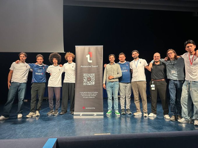 Nine men pose together on a stage flanking a banner that reads 'Avalanche Team1' with a QR code and 'x_avalaiche' handle.