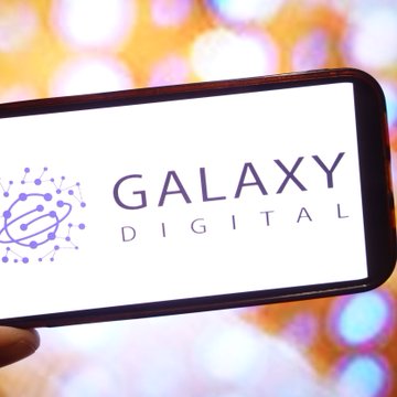 A smartphone displays the Galaxy Digital logo on its screen against a blurred bokeh background.
