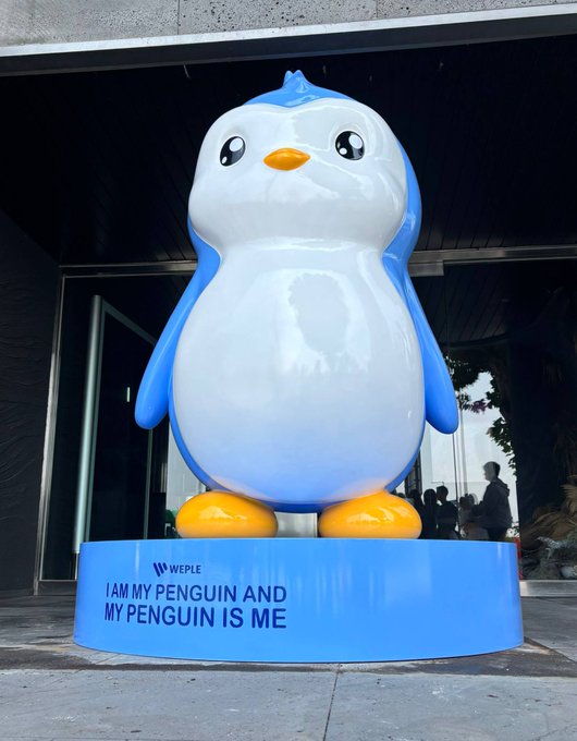 The image features a large, blue and white penguin statue standing on a pedestal or base. The penguin has yellow feet and a blue body with a blue head. In front of the penguin, there is text that reads "I am my Penguin and My Penguin is Me". This suggests that the penguin might be part of an art installation or sculpture dedicated to celebrating the unique characteristics of this particular penguin species.