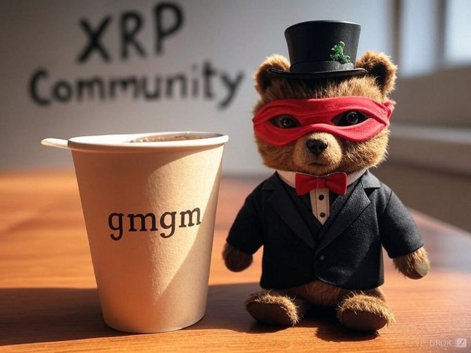 A teddy bear dressed as a gentleman in a black suit, top hat with a green clover, and red masquerade mask, sitting next to a paper cup labeled 'gmgm' with 'XRP Community' written on the wall behind it.