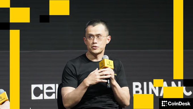 Photo of Binance founder Changpeng Zhao speaking at a CoinDesk event, wearing a black t-shirt and holding a microphone with a Binance-branded yellow mic flag.