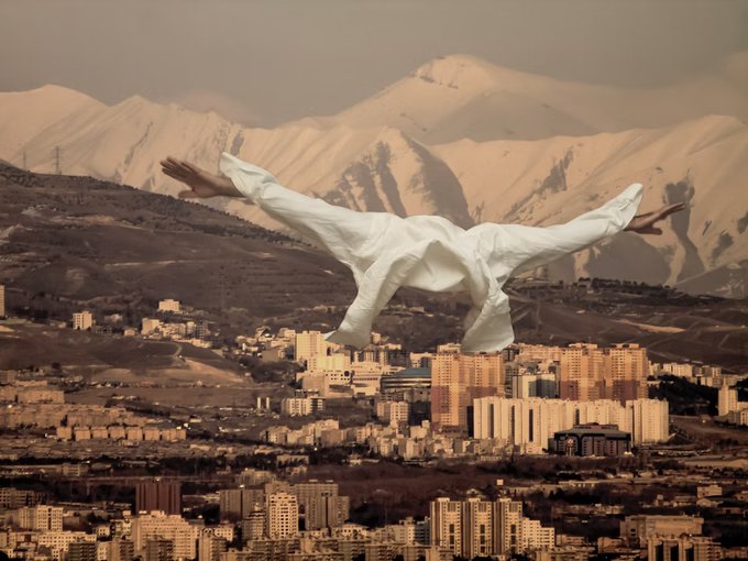 A surreal composite image showing a person in a white shirt floating horizontally over a sprawling cityscape with snow-capped mountains in the background.