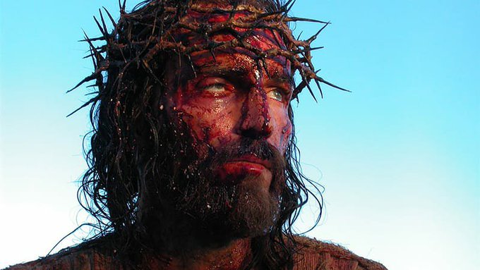 A close-up of a man wearing a crown of thorns, with blood-streaked, weathered skin and a pained yet resolute upward gaze against a pale blue sky, evokes a religious tone of faith and sacrifice. The image aligns with the post's message of placing Jesus above all worldly concerns, contrasting spiritual steadfastness with the fleeting nature of financial gain and XRP speculation.