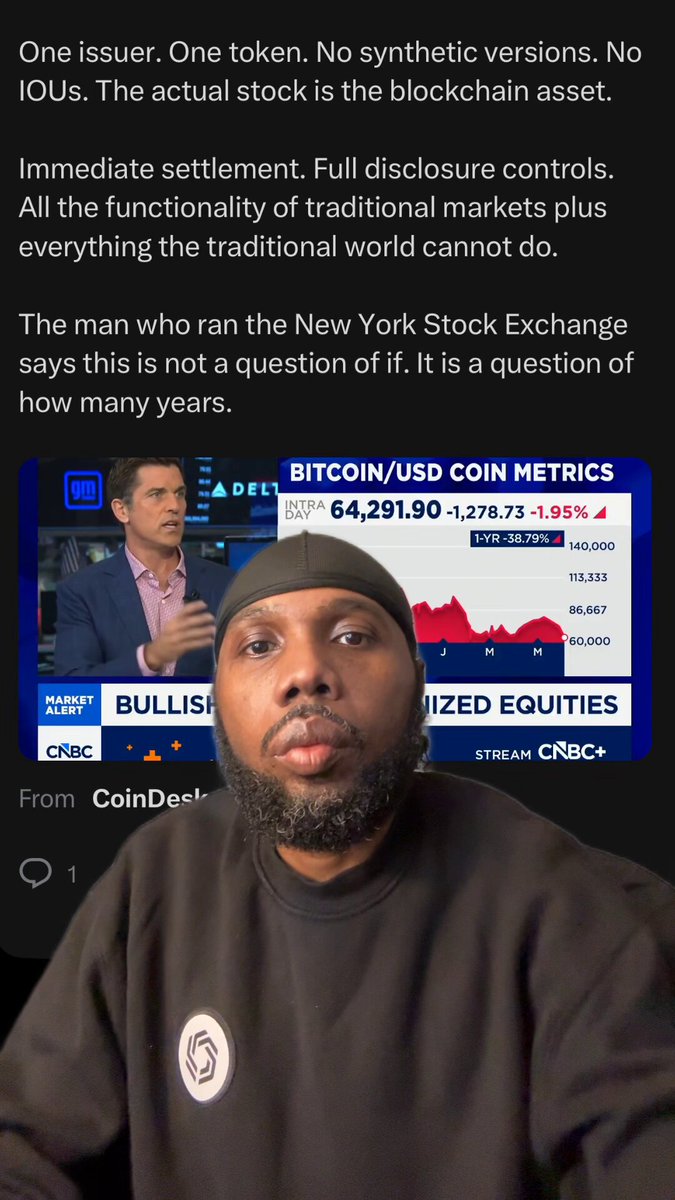 The image features a man with a shaved head wearing a black sweatshirt sitting down. There are two computer monitors present, one directly above him and another that appears to be placed behind his back or slightly elevated. The first monitor displays information about Bitcoin and the stock market, while the second monitor shows two different headlines: "One issue, one token. No synthetic versions. No ious. The actual stock asset..." and a man talking on the phone with the same content displayed on this screen.