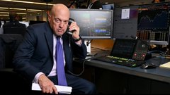 A stock photo of a bald businessman in a suit talking on a landline phone in an office setting.