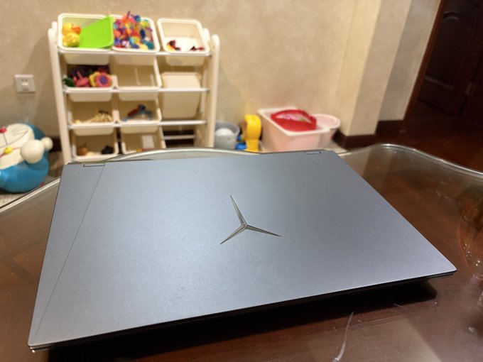 A closed gray laptop with a Mercedes-Benz logo sits on a glass table in a home setting with a child's toy organizer visible in the background.