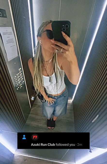 A mirror selfie of a woman with long blonde braids wearing sunglasses, a white tank top, and denim shorts, with a notification showing 'Azuki Run Club followed you · 2m'.