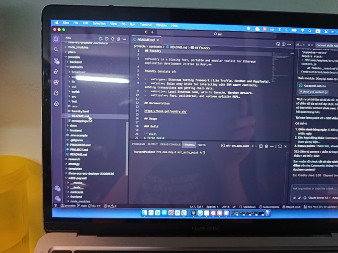 The image shows an open laptop screen displaying code or text that appears to be related to smart contracts. The laptop's screen has a purple background, which contrasts with the yellow cup sitting next to it. The text on the screen seems to be about building something fun using smart contracts and includes details such as the name of the project and its progress. The overall atmosphere suggests an engaging and creative process involving programming or coding.