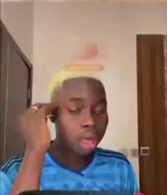 A low-quality video still of a young person in a blue striped shirt sitting indoors, with what appears to be a blurry object or figure superimposed above their head.