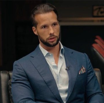 A man in a blue suit jacket and white shirt, identified as Tristan Tate by the post's quote, speaks during an interview setting. The caption alongside his image presents a bold statement about accumulating 21 Bitcoin as a path to joining the top 1% financially.