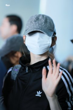 A person wearing a gray cap and white face mask waving, dressed in a black Adidas track jacket with white stripes.