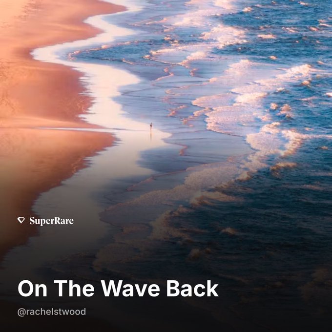 An aerial photograph titled 'On The Wave Back' by @rachelstwood, tagged as 'SuperRare', showing a small figure standing at the shoreline where pink-tinted sand meets foamy blue waves.