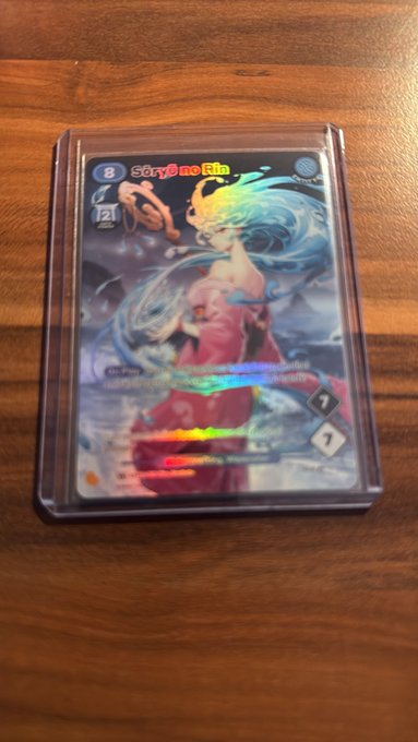 A holographic Pokémon TCG card featuring the character Scarlet & Violet in a protective sleeve resting on a wooden surface.