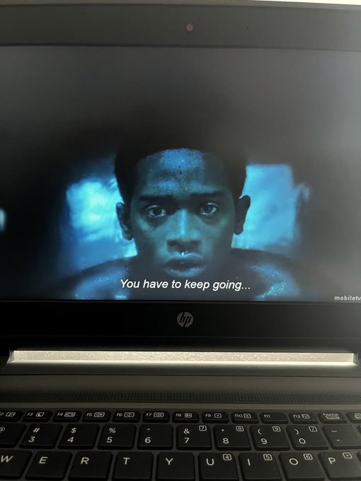 A laptop screen displays a dark, intense scene featuring a man with a determined expression and the subtitle "You have to keep going..."—a visual echo of the motivational post's message about perseverance: "The only way out is through."