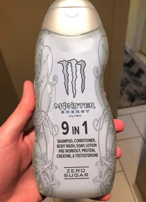 A hand holds a silver Monster Energy Ultra '9 in 1' shampoo/body wash bottle, claiming to contain shampoo, conditioner, body wash, soap, lotion, pre-workout, protein, creatine, and testosterone, and is zero sugar.