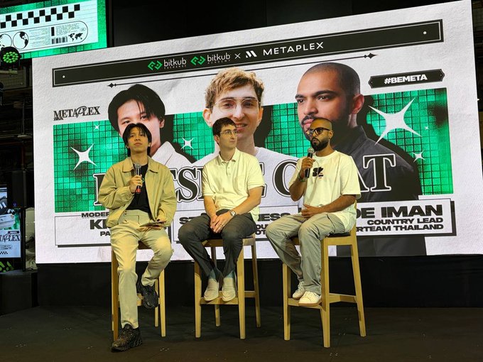 Three men sit on stools on a stage in front of a large screen displaying 'bitkub x METAPLEX' branding and '#BEMETA' with portraits of the speakers, appearing to be at a press conference or panel discussion.