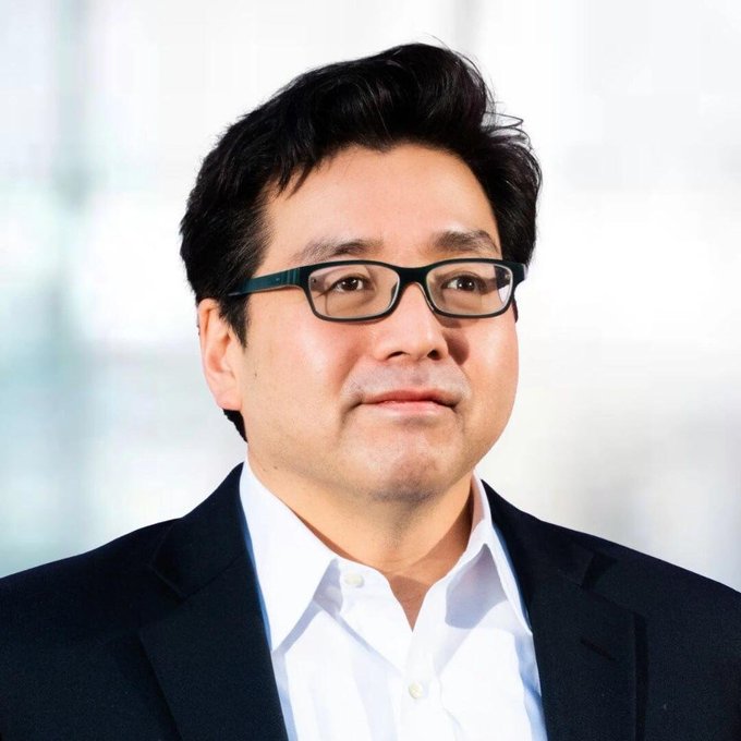 A professional headshot of a middle-aged Asian man with dark hair, wearing black-framed glasses, a white collared shirt, and a dark blazer, likely depicting Tom Lee in the context of his Bitmine-related ETH purchase.