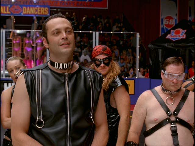 The image shows a man with a leather jacket standing between two other men wearing leather outfits, possibly part of some subculture or group activity. The three people seem to be taking a break from their performance to interact with each other. There are no other objects in the scene that are relevant to the context or could provide additional information about what is happening in the image.