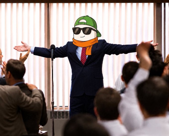 A man in a business suit with a green cap, sunglasses, and an orange scarf stands at a microphone with arms outstretched before a crowd of applauding people, as the post "I feel it" expresses the euphoric energy of the moment.