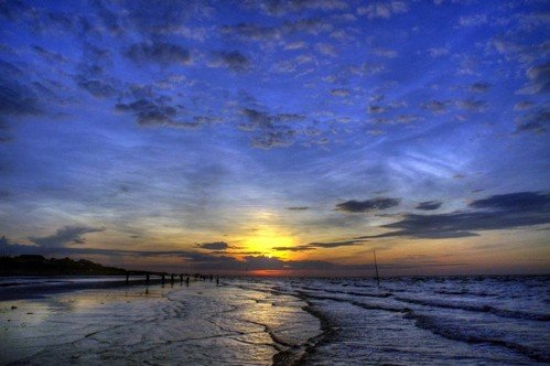 A scenic sunset over a beach with calm waves reflecting the golden light under a sky filled with scattered clouds.