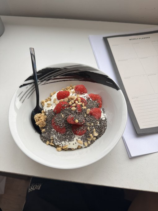 A bowl of yogurt topped with chia seeds, raspberries, and granola sits beside a "WEEKLY PLANNER" notebook, styled to evoke a productive morning routine that aligns with the post's pitch to follow an unemployed lifestyle account and share a SOL wallet.