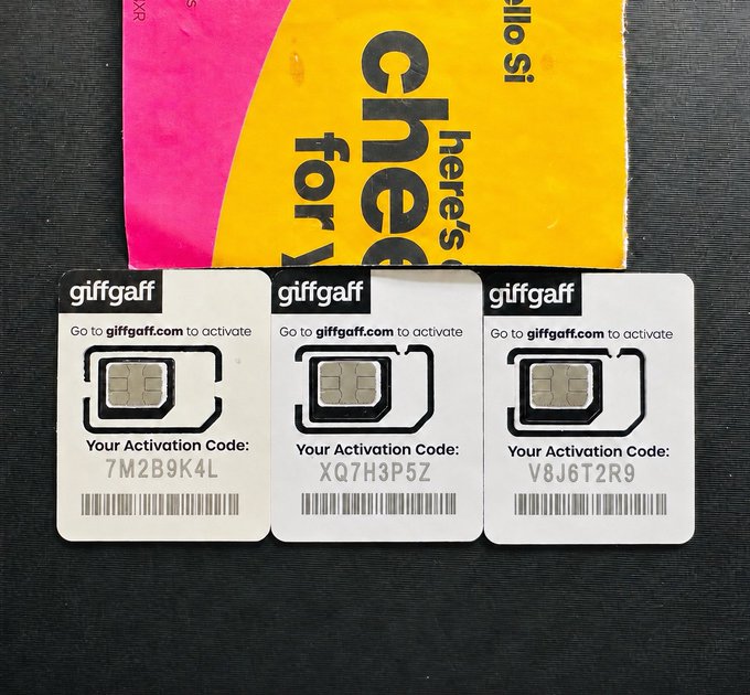 Three small white Giffaf activation cards with black text and numbers are arranged on a black surface, accompanied by a pink and yellow flyer for Giffaf.
