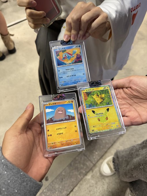 Three Japanese Pokémon trading cards (Wobbfet, Pikachu, and Dugtrio) displayed in protective cases held by different people.