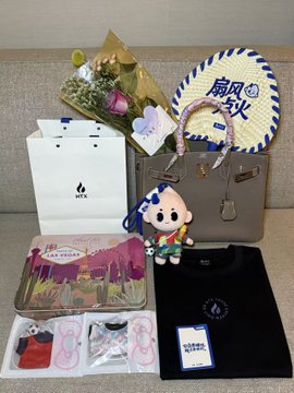 A collection of prizes and souvenirs from a US trip arranged by HTX_Global, including a tote bag, a decorative uchiwa fan with "扇田秋" (Sensuaki) text, a flower bouquet, a plush mascot doll, a gray handbag, and other gift items packaged in branded boxes. The image showcases the abundance of gifts received from the trip, aligning with the post's mention of "plenty more surprises" and the anticipation for more on-site photos from "Little K."