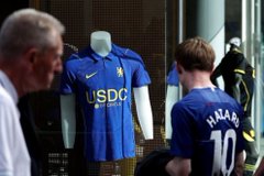 The image shows a young boy gazing at a Chelsea FC jersey displayed on a mannequin, with "COOL" branded across the front and another jersey hanging nearby featuring the name "HAZARD" and the number 10 on the back. The scene captures the excited anticipation of a young fan eagerly awaiting match day while admiring his team's merchandise.