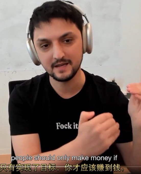 A man with a beard wearing headphones and a black t-shirt that says 'Fock it' gestures while speaking, with subtitles reading 'people should only make money if' in English and Chinese.