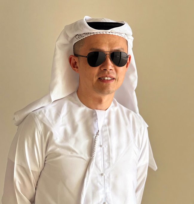A man wearing traditional white Arab attire (kandura and ghutra) and dark aviator sunglasses.