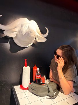A woman sits at a tiled restaurant table talking on the phone, with a white octopus-shaped wall decoration and condiment bottles nearby.