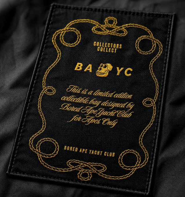 A black fabric patch features gold embroidered text reading "COLLECTORS COLLECT BAYC" with a skull replacing the "A," along with a message stating "This is a limited edition collectible bag designed by Bored Ape Yacht Club for Apes Only" and "BORED APE YACHT CLUB," framed by ornate gold rope detailing—serving as authentic Bored Ape Yacht Club merchandise branding.