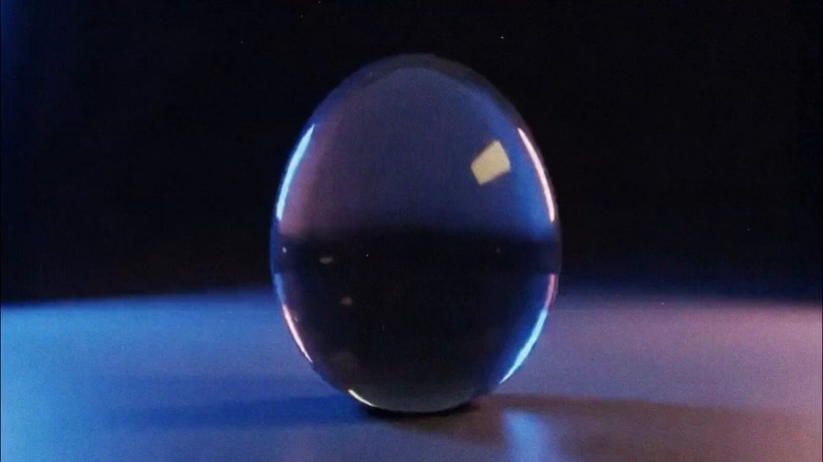 The image depicts a large, round glass ball sitting against a dark background. The ball appears to be floating or resting peacefully at the center of attention. Below the image, there's text that reads: "$50K earned on @contra - Grateful for every client who trusted me, every project that pushed me, and every lesson along the way." This message is placed directly below the glass ball, emphasizing its significance in the overall composition of the post.