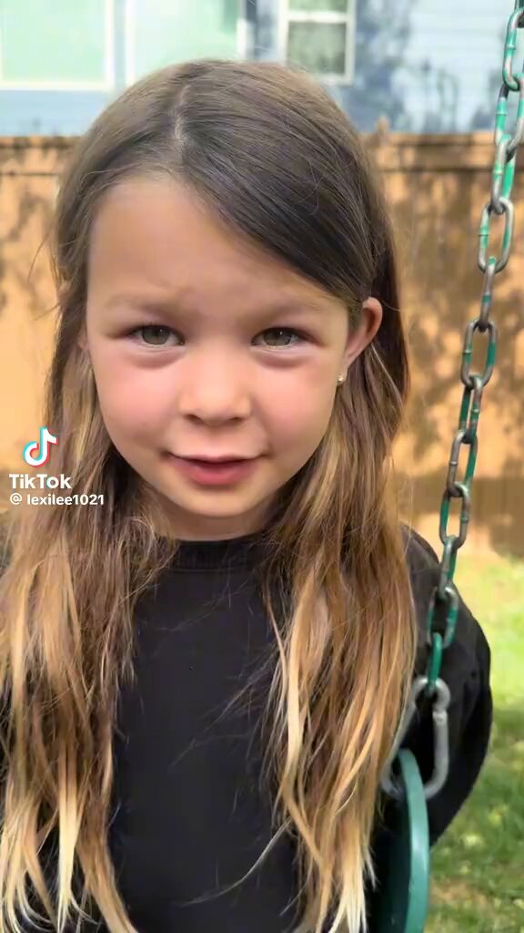 iced tea with a straw, a green swing set, and a chain link fence are present in the background of a photo featuring a young girl's face.