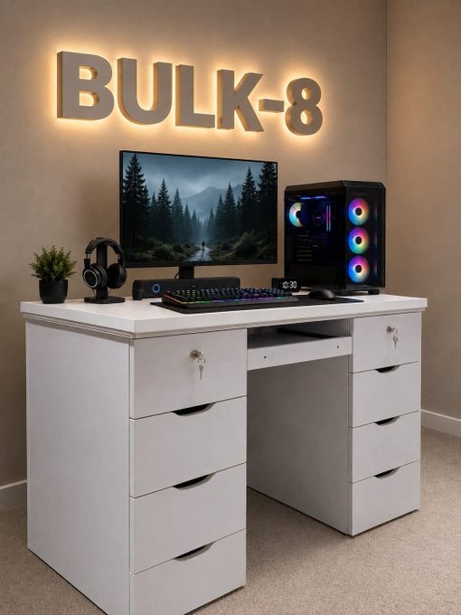A white gaming desk setup labeled 'BULK-8' in illuminated wall letters, featuring a monitor, RGB PC tower, headphone stand, and digital clock.