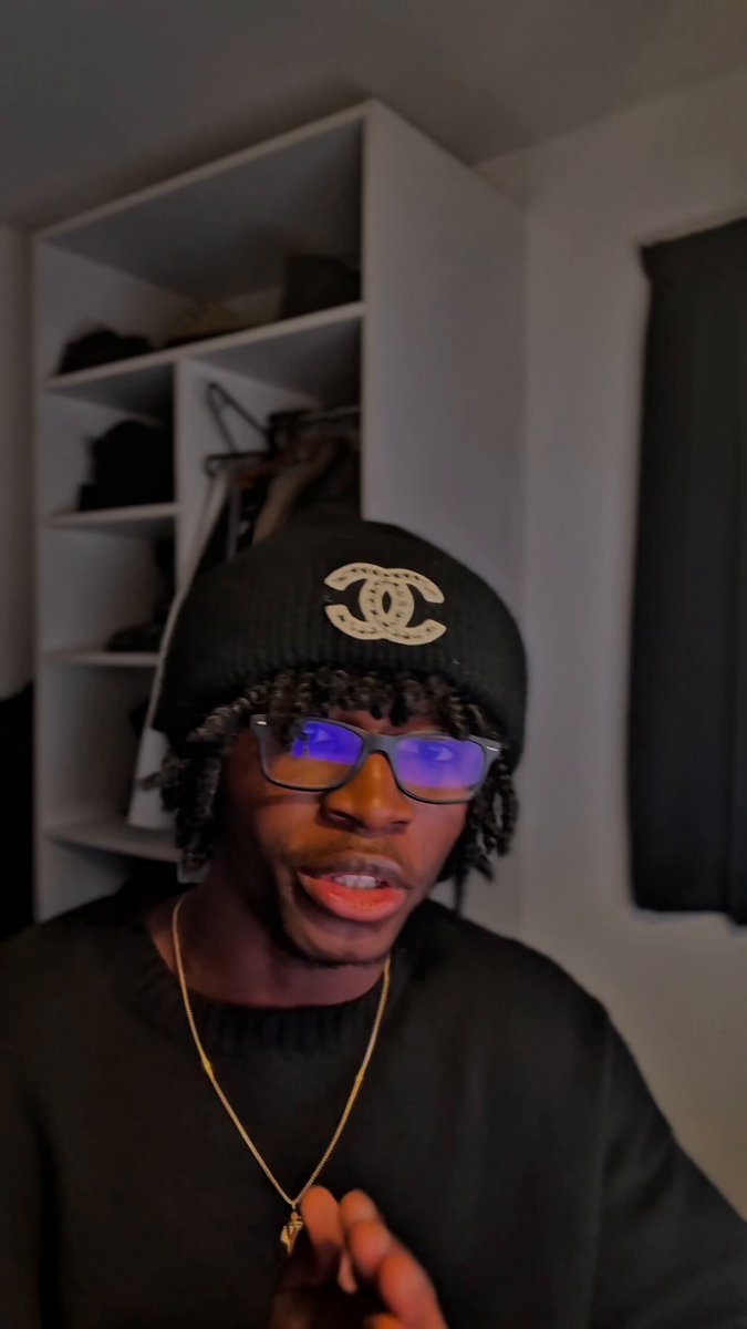 The image features a man wearing glasses and a black hat with a "Chanel" logo, sitting down in front of a white wall. The man appears to be posing for a photo or video, possibly for a social media platform like Instagram.