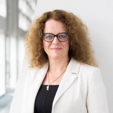 A professional portrait shows a woman with curly blonde hair, glasses, and a white blazer over a black top, standing against a bright, minimalist background. The image appears to be a headshot of Isabel Schnabel, the ECB board member referenced in the post advocating for central banks to adopt blockchain technology.