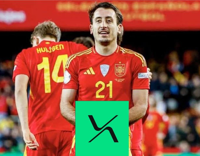 Spanish footballer Mikel Oyarzabal, wearing the number 21 Spain national team jersey, smiles on the pitch with teammate Huijsen (#14) visible behind him.